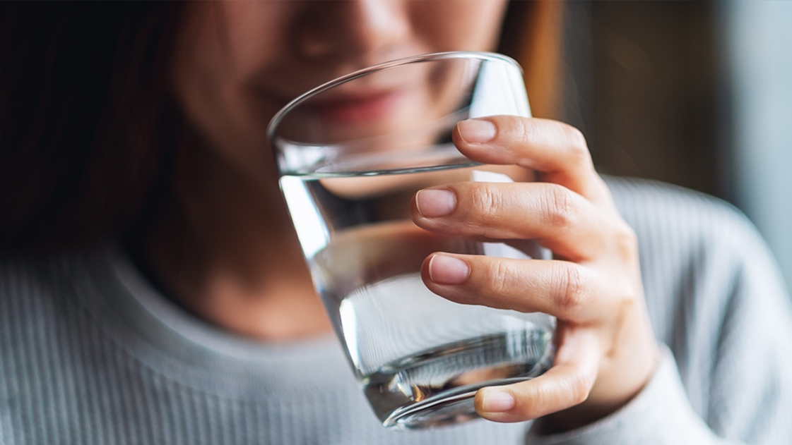 A woman drinks water from a glass. 